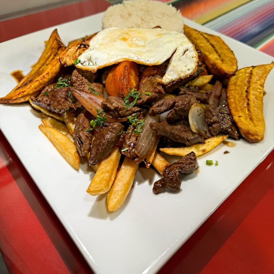 Peruvian Lomo Saltado with beef, fries, plantains, rice, and a fried egg on a white plate.