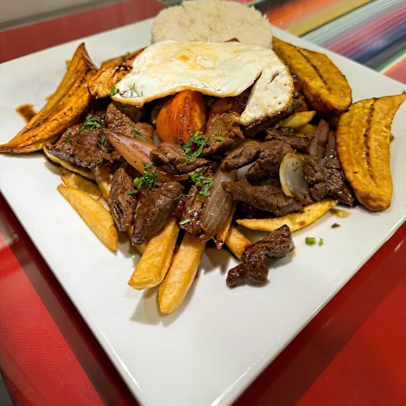 Peruvian Lomo Saltado with beef, fries, plantains, rice, and a fried egg on a white plate.