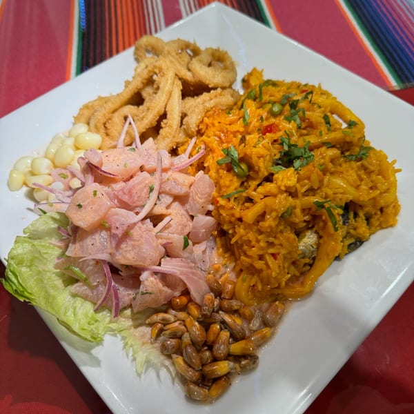 A Peruvian dish with ceviche, fried calamari, yellow rice, corn, and lettuce on a white plate.