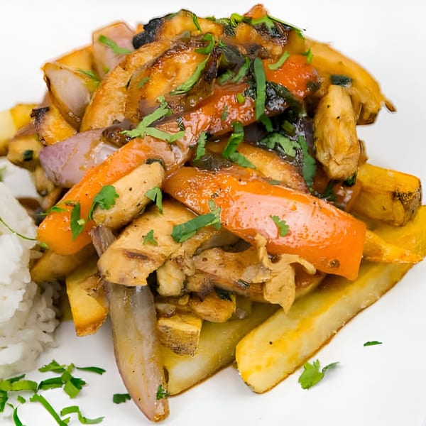 Peruvian Lomo Saltado with beef, onions, tomatoes, and French fries, garnished with cilantro and rice.