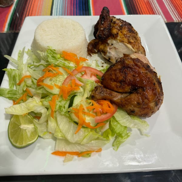 Peruvian grilled chicken with white rice, a fresh salad, and a lime wedge on a white plate.
