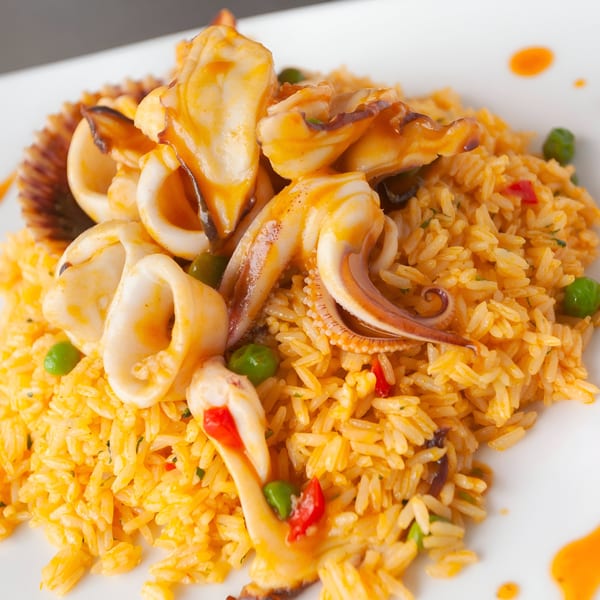 Peruvian arroz con mariscos, featuring rice, squid, and a scallop on a white plate.
